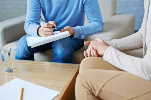 A man and woman on a couch, collaborating on a project with a pen and paper in hand, deep in conversation.