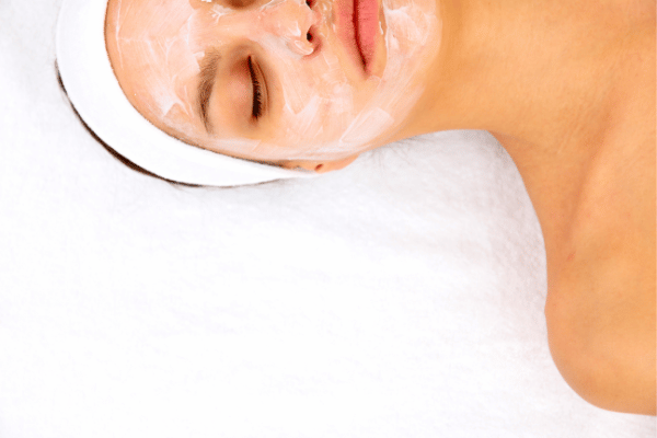 A woman lying on a towel, enjoying holistic facial therapy with a soothing facial mask on her face.