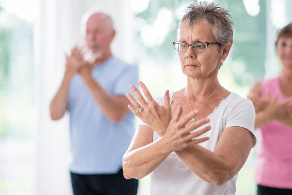 A group of individuals, including an older woman, engage in tai chi exercises in a peaceful environment.